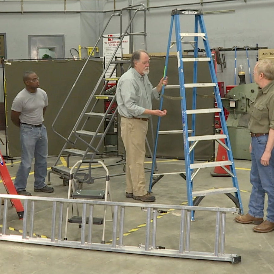 Group of people in a workshop setting with ladders and safety equipment.
